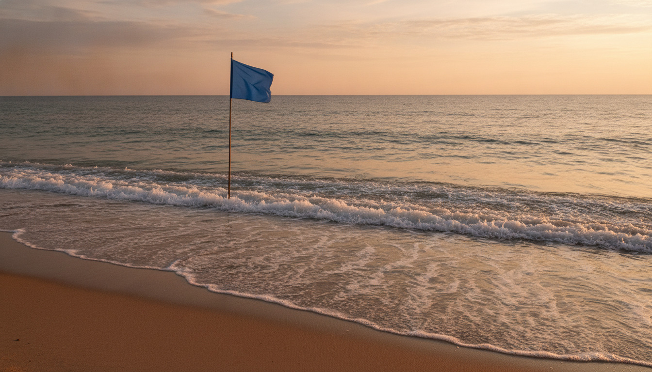 Tæt på: blå flag og ølende sandstrand med bølger ved solnedgang.
